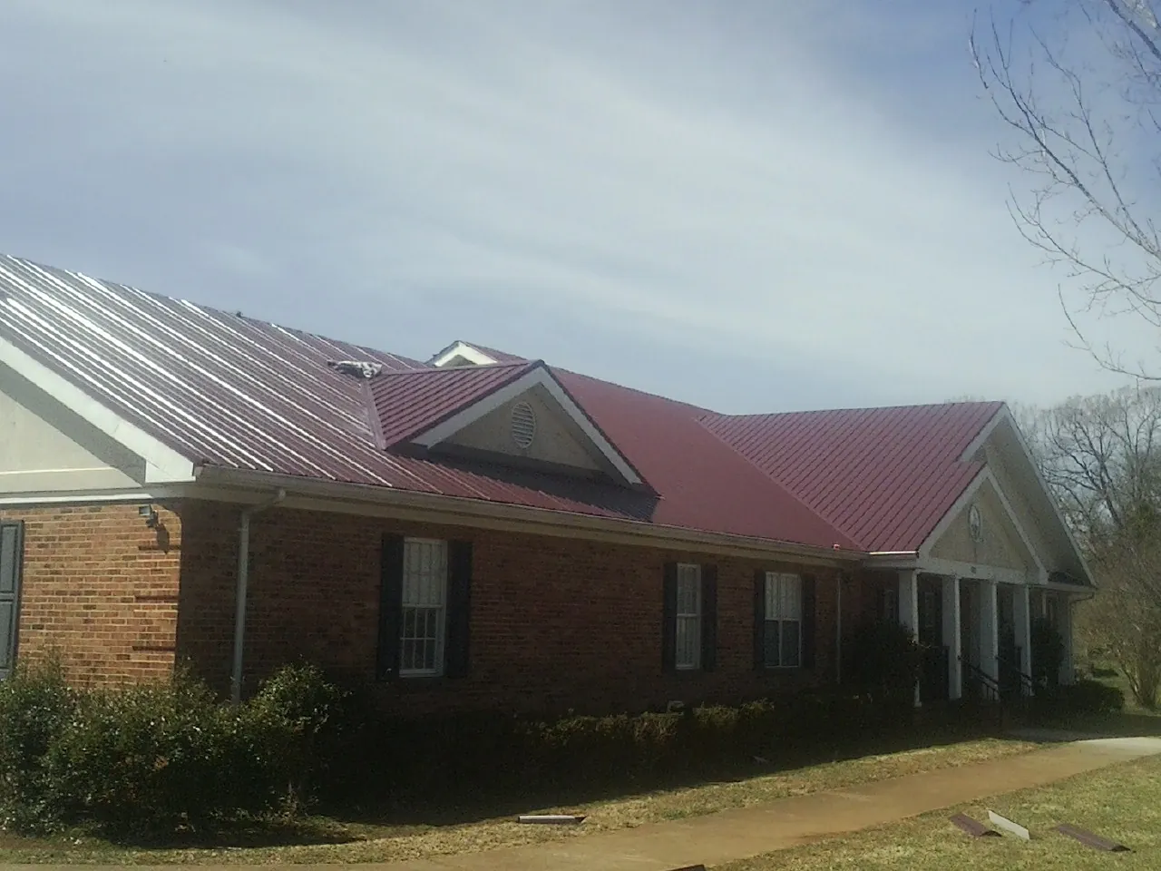 Red metal roof with gabled entries on a long brick building, from a Hail Damage Roof Repair job in Dyersburg