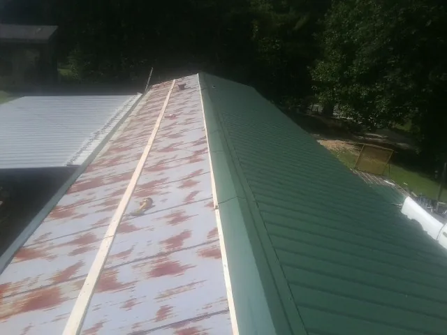 Old rusted panels beside newly installed green metal roofing — Wind Damage Roof Repair by Roofing Brothers in Dyersburg