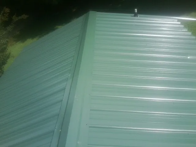 New green metal panels meeting at the ridge of a roof — Flat Roof Repair work by our crew in Dyersburg