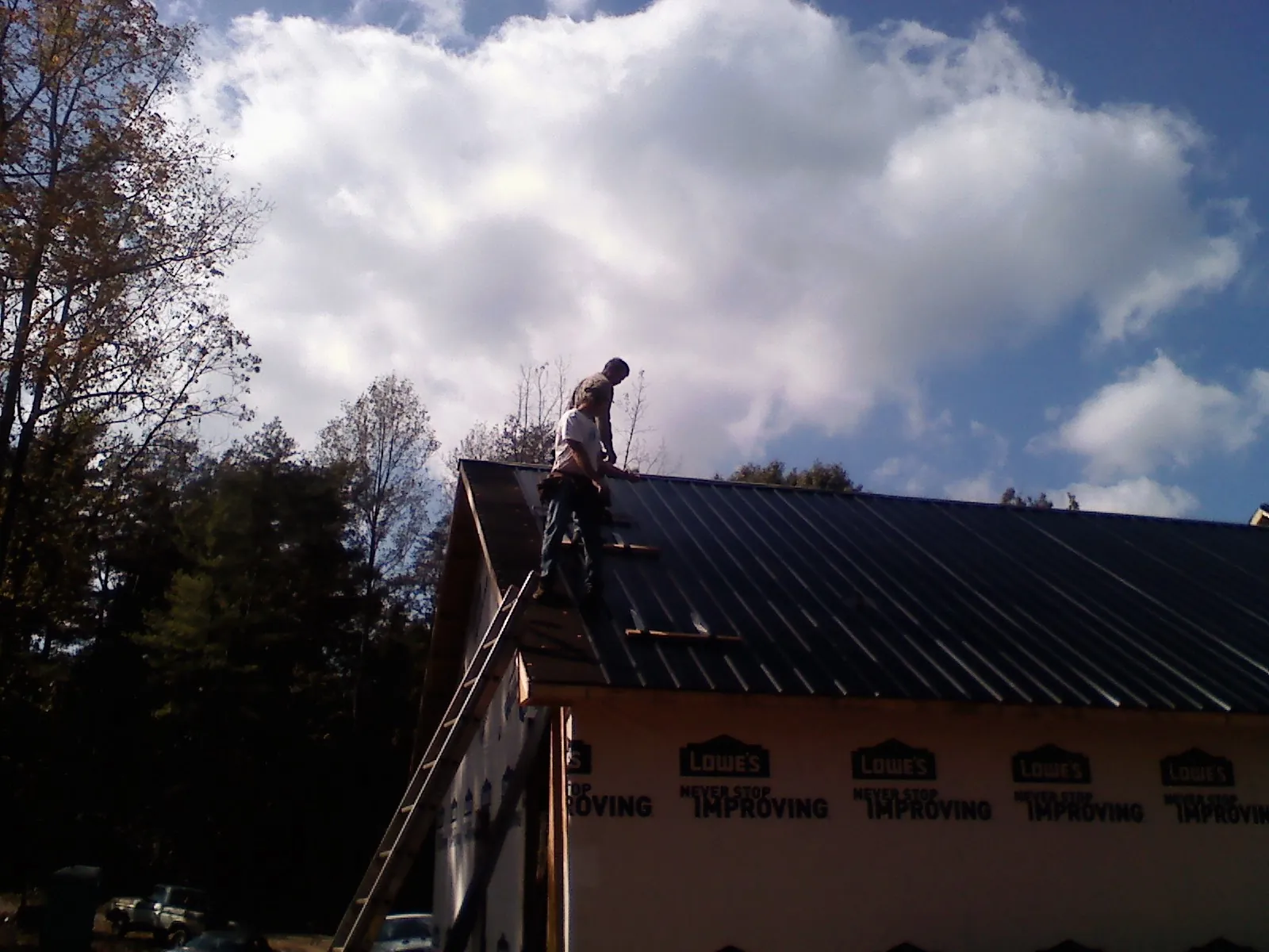 Roofer fastening dark metal panels high against a cloudy sky, from a Roof Inspection job in Dyersburg