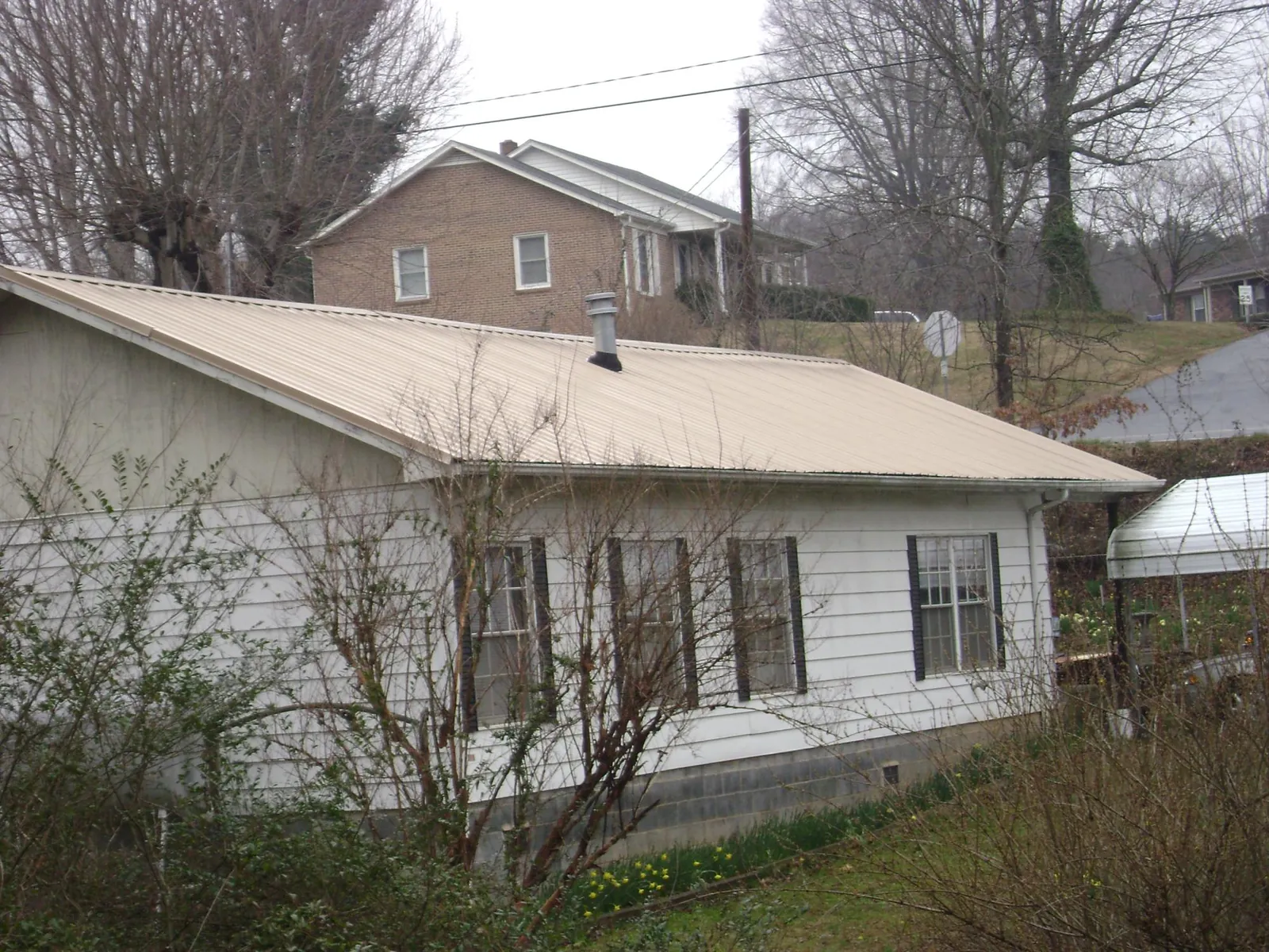 Tan metal roof on a white sided house set into a hillside — Commercial Roofing by Roofing Brothers in Dyersburg
